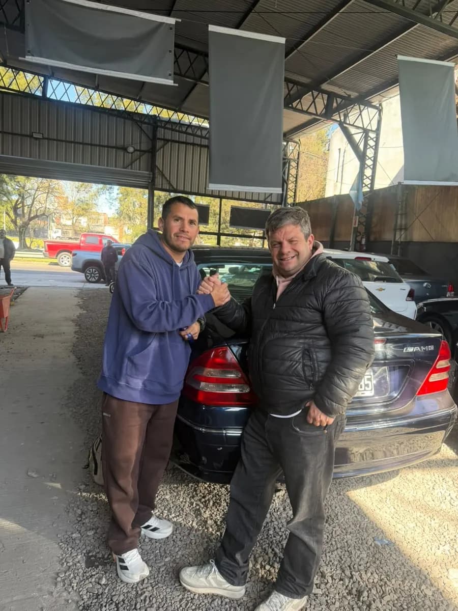 Juan Manuel y un cliente se dan la mano delante de un Mercedes-Benz negro, en el local