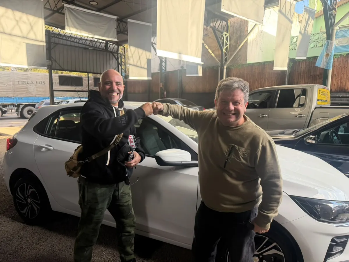 Juan Manuel y un cliente chocan los puños junto a un auto blanco, en el local